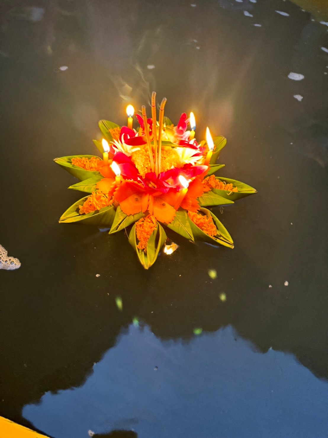 A lit Krathong floating on dark water at night